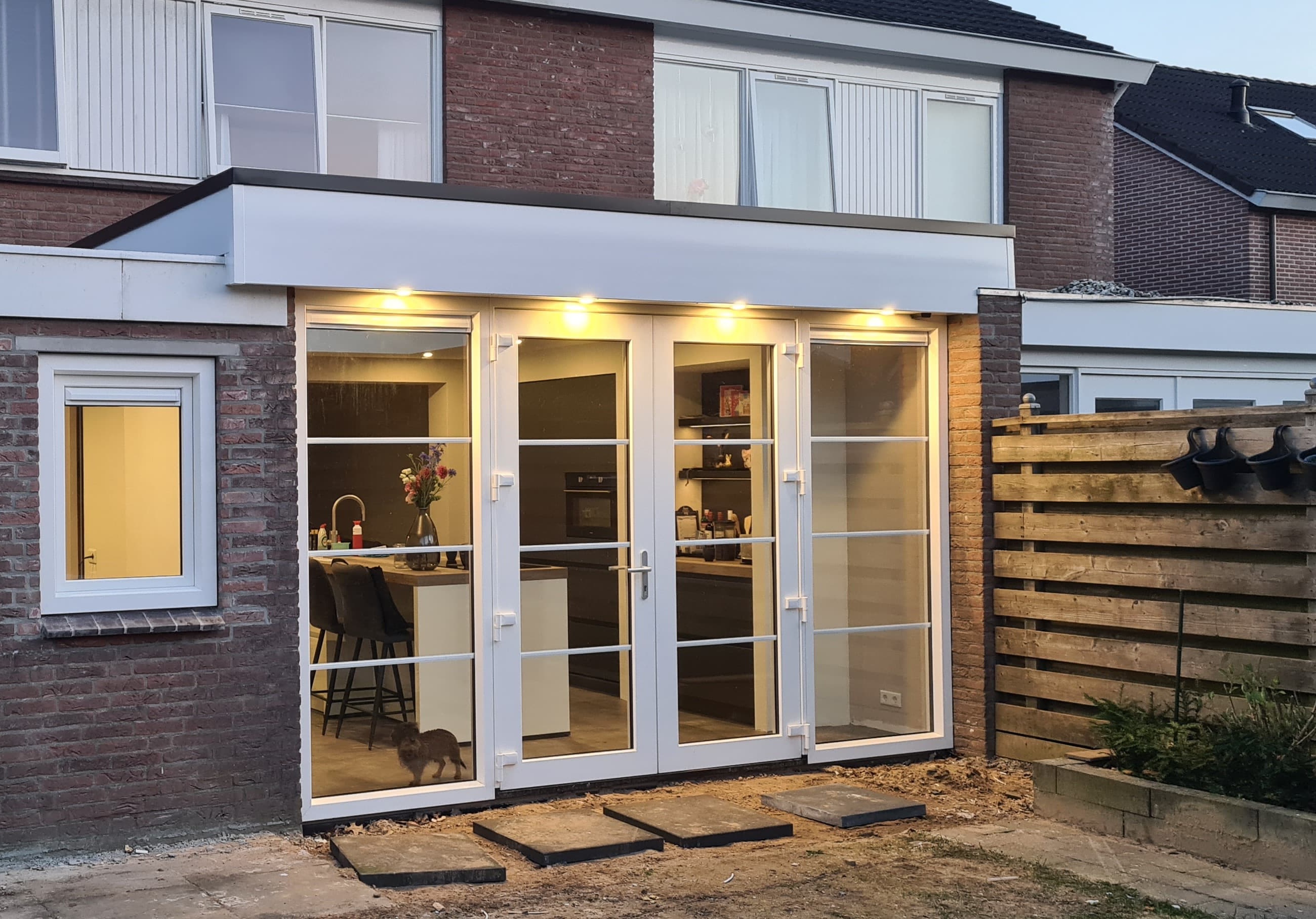 Buitenkant van een uitbouw met verlichte pui en openslaande tuindeuren